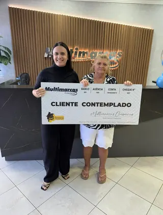 Cliente contemplada nº 1 pelo consórcio, segurando o cheque simbólico da carta de crédito