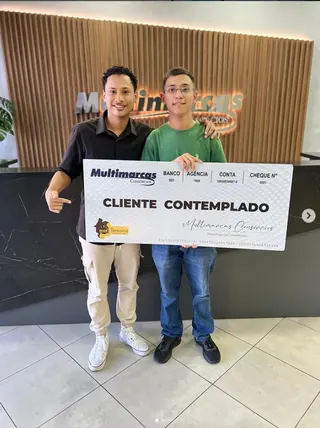 Cliente contemplado nº 10 pelo consórcio, segurando o cheque simbólico da carta de crédito