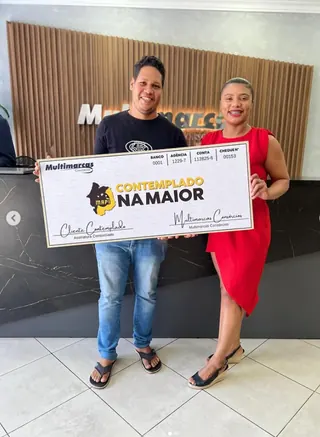 Cliente contemplado nº 11 pelo consórcio, segurando o cheque simbólico da carta de crédito