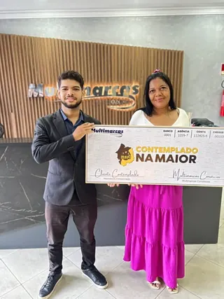 Cliente contemplado nº 2 pelo consórcio, segurando o cheque simbólico da carta de crédito