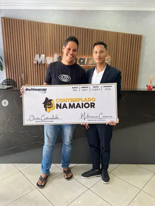 Cliente contemplado nº 4 pelo consórcio, segurando o cheque simbólico da carta de crédito