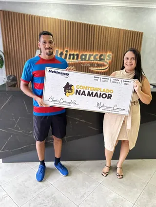 Cliente contemplado nº 6 pelo consórcio, segurando o cheque simbólico da carta de crédito